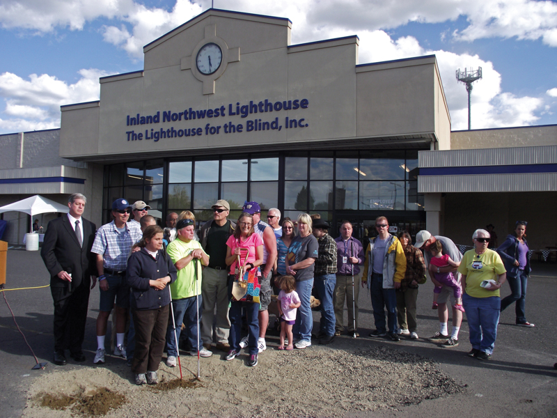 group photo of Spokane Lighthouse employees breaking ground using a ceremonial entrenchment tool in the parking lot of the facility